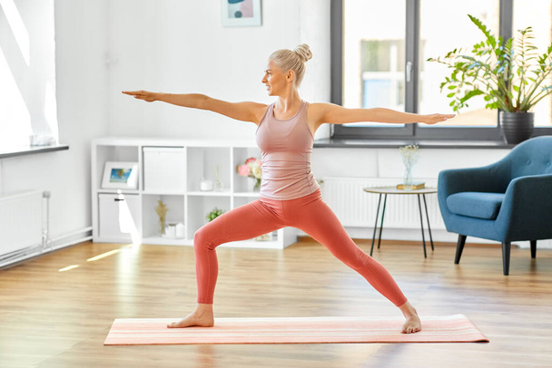 vrouw doet yoga krijger pose thuis - Foto, afbeelding