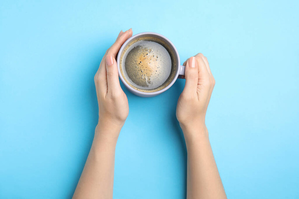 Woman with cup of coffee on light blue background, top view - Foto, afbeelding