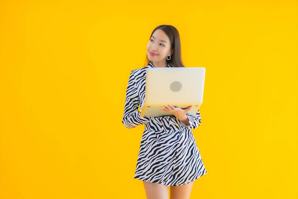 Portré gyönyörű fiatal ázsiai nő használ laptop számítógép sárga elszigetelt háttér - Fotó, kép