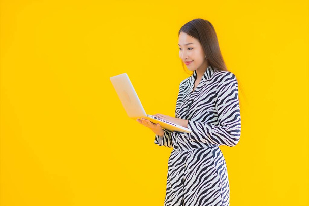 Retrato hermosa joven mujer asiática uso ordenador portátil en amarillo aislado fondo - Foto, imagen