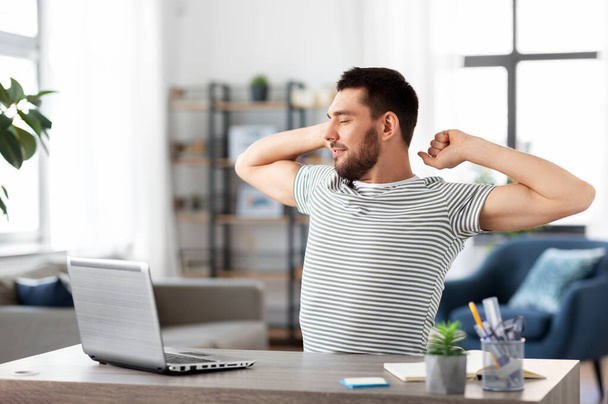 happy man with laptop stretching at home office - Фото, изображение