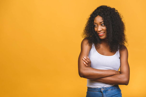 Portrait of beautiful positive african american black woman standing with arms crossed isolated over yellow background.  - Фото, изображение