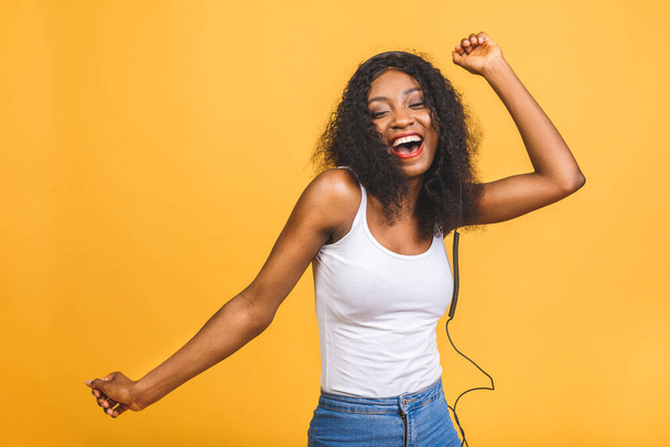 Photo studio d'une femme afro-américaine inspirée écoutant de la musique, dansant les yeux fermés. Portrait intérieur de fille noire détendue isolée sur fond jaune. - Photo, image