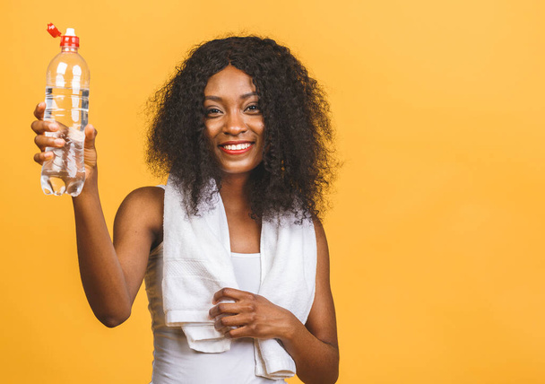 Beautiful attractive young sweaty african american black woman drinking water after exercise workout, rehydrating thirst quenching, isolated over yellow background. - Фото, зображення