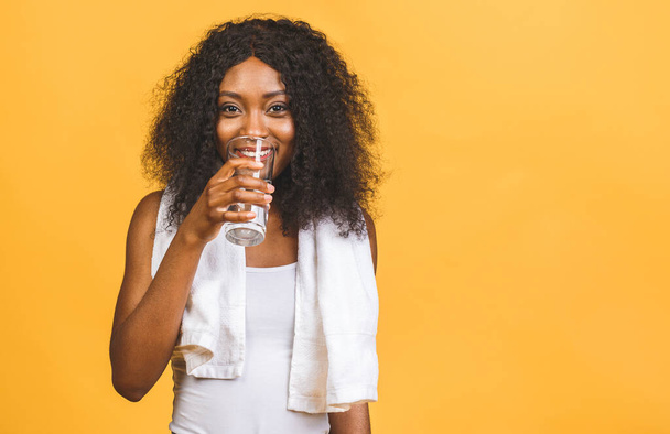 Gyönyörű vonzó fiatal izzadt afro-amerikai fekete nő ivóvíz edzés után, rehidratáló szomjúság oltó, elszigetelt sárga háttér. - Fotó, kép