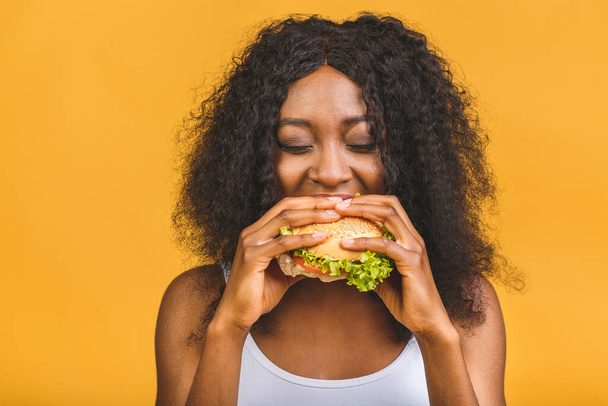 African American black beautiful young woman eating hamburger isolated on yellow background. - Foto, imagen