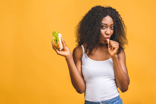 Afroamerikaner schwarz schöne junge Frau essen Hamburger isoliert auf gelbem Hintergrund. - Foto, Bild