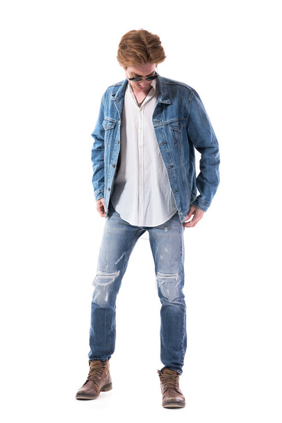Hezký mladý stylový muž zkouší nové džínové sako shlížející dolů. Plná délka těla izolované na bílém pozadí.  - Fotografie, Obrázek