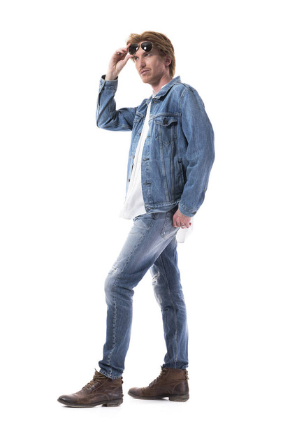 Macho fotogénico elegante hombre fresco en jeans con gafas de sol mirando hacia arriba. Longitud total del cuerpo aislado sobre fondo blanco
.  - Foto, imagen