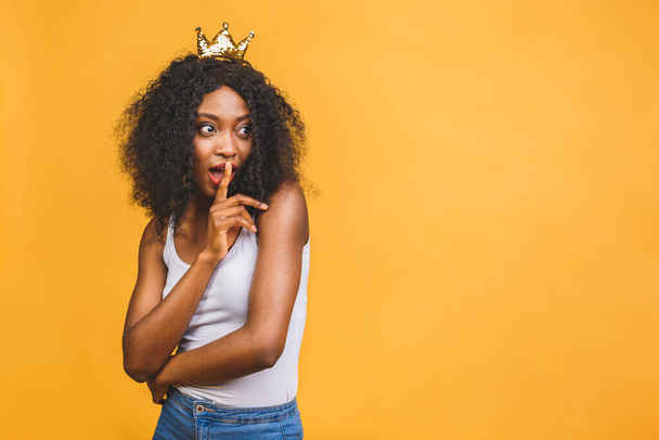 Afrikalı 20 'li yaşlarda sıradan giyinen, dudağında işaret parmağı olan ve sarı arka planda sessiz kalmak isteyen bir kadın resmi.. - Fotoğraf, Görsel