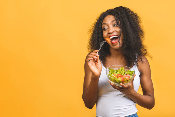 Gezond voedsel concept. Close-up van mooie Afro-Amerikaanse zwarte vrouw eten salade geïsoleerd over gele achtergrond.  - Foto, afbeelding