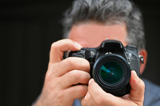 Fotógrafo homem fotografando com uma câmera isolada em fundo preto
. - Foto, Imagem