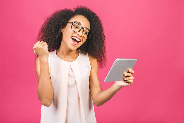 Happy african american girl looking excited looking at her tablet screen celebrating victory making winner gesture screaming and laughing. Success, happiness, joy concept. - Foto, imagen