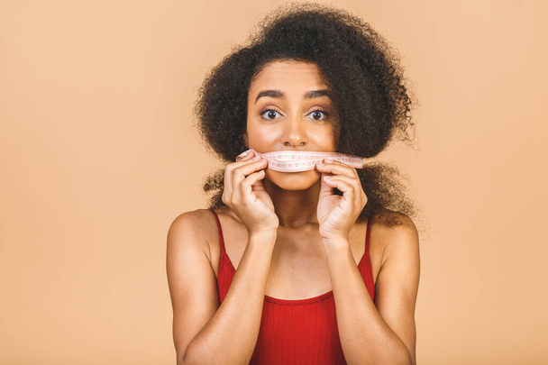 Dieting concept. Slim shocked amazed african american woman shows centimeter isolated over beige background.  - 写真・画像