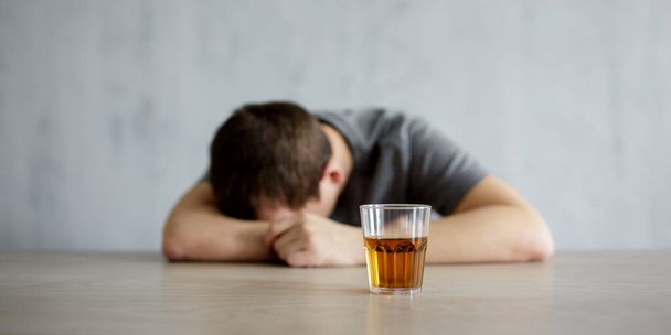 アルコール依存症の概念-灰色の壁の背景にウイスキーのテーブルとガラスの上に横たわる酔った男 - 写真・画像