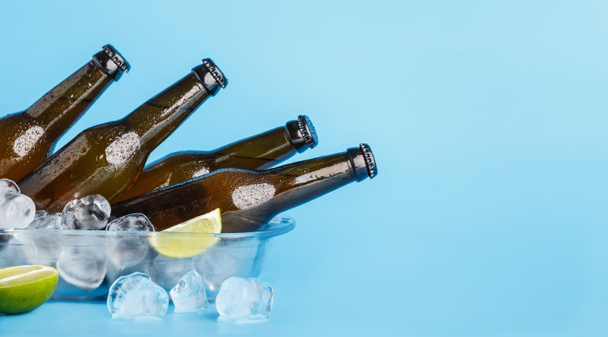 Friss sör a forró napon. Sötét üvegpalackok üvegtálcában, kék alapon, jéggel és lime-mal - Fotó, kép