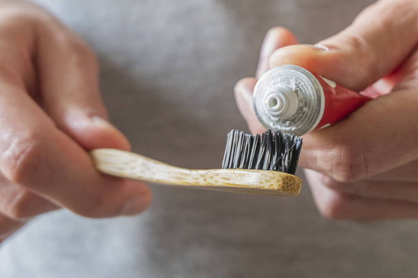Mãos masculinas aplicando pasta de dentes na escova de dentes de bambu natural eco. Zero resíduos em casa, itens livres de plástico
 - Foto, Imagem