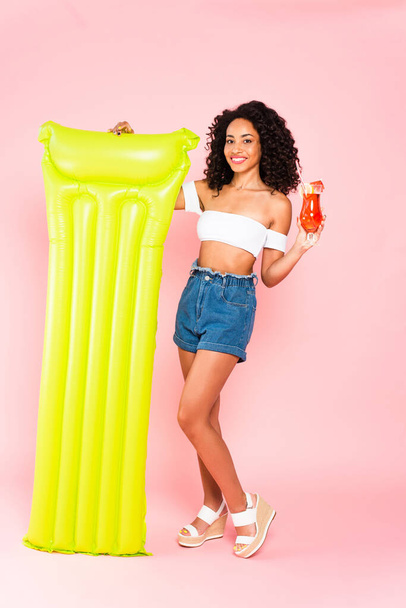 happy african american girl holding cocktail and inflatable mattress on pink  - Fotó, kép