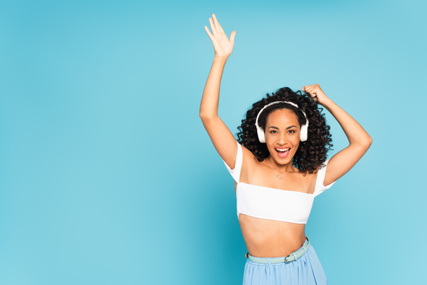 chica afroamericana emocionada escuchando música en auriculares inalámbricos y bailando en azul
  - Foto, imagen
