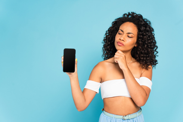 pensive african american girl looking at smartphone with blank screen isolated on blue  - Foto, immagini