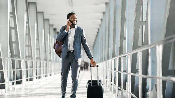 Cheerful Black Businessman Chatting On Phone Walking In Airport, Panorama - Foto, Bild