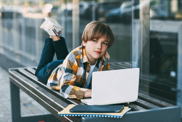 A smiling boy is lying on a bench and preparing for school lessons, next to a backpack. The boy is resting between classes. Social distance. Distance learning, education, - Foto, imagen