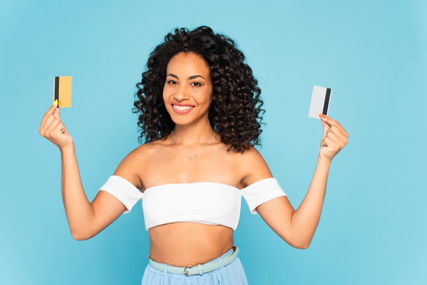 mulher americana africana alegre segurando cartões de crédito isolados em azul
  - Foto, Imagem