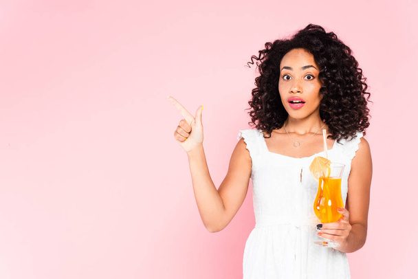 surprised african american girl pointing with finger and holding cocktail on pink  - Фото, изображение