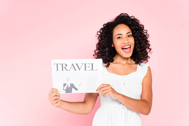 excitada chica afroamericana sosteniendo periódico de viaje aislado en rosa
  - Foto, Imagen