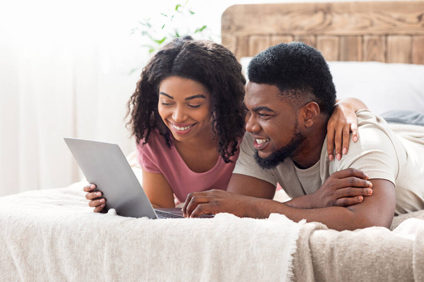 Relaxed african man and woman resting at bedroom, using laptop - Fotó, kép