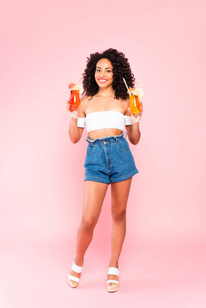 smiling african american woman standing and holding cocktails on pink  - Foto, Imagem
