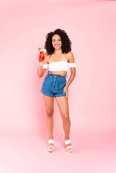 smiling african american woman standing and holding cocktail on pink  - Foto, Imagem