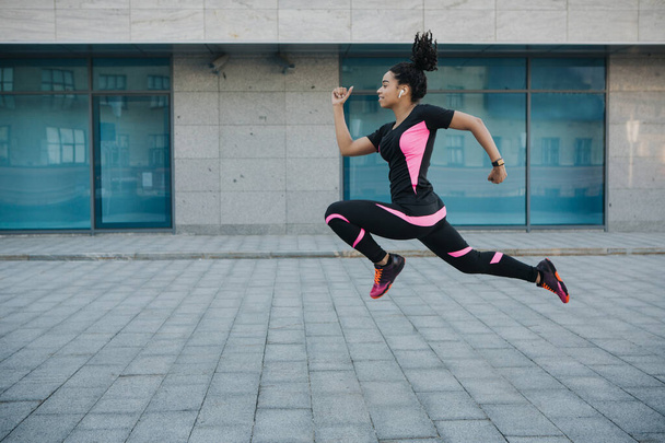 Bewegung zur Gewichtsabnahme. Frau in Sportbekleidung mit kabellosen Kopfhörern, die in der Luft erstarrt sind und beim Laufen springen - Foto, Bild