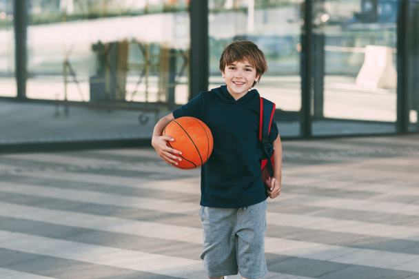 A cheerful boy with a backpack and a basketball. A boy hurries to basketball practice. Training, education - Zdjęcie, obraz