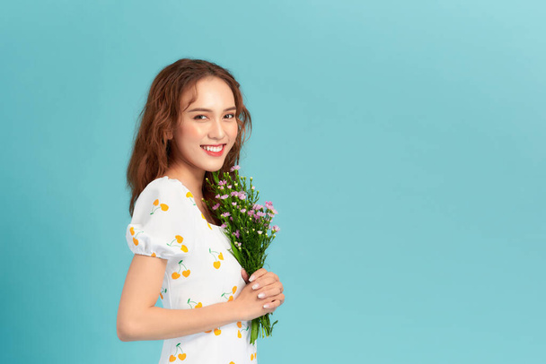 Portrait of a cheerful pretty woman holding flowers over blue background - Photo, Image