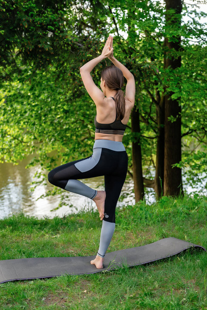 una jovencita se dedica al yoga, se para en una pose de árbol sobre la naturaleza en verano - Foto, Imagen
