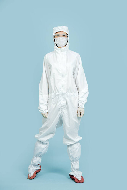 Fully geared up woman doctor posing for a photo in a white costume covering all skin. She's wearing mask, gloves and glasses. Prepared for virus outbreak. - 写真・画像