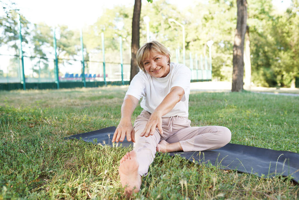 Νεαρή υγιής γυναίκα κάνει ασκήσεις τέντωμα στο γρασίδι σε εξωτερικούς χώρους. - Φωτογραφία, εικόνα