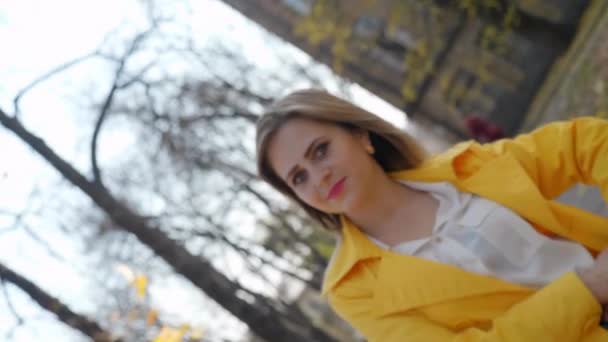 Donna in mantello giallo, camicetta sorride, stand parco autunnale, guarda telecamera ruota - Filmati, video