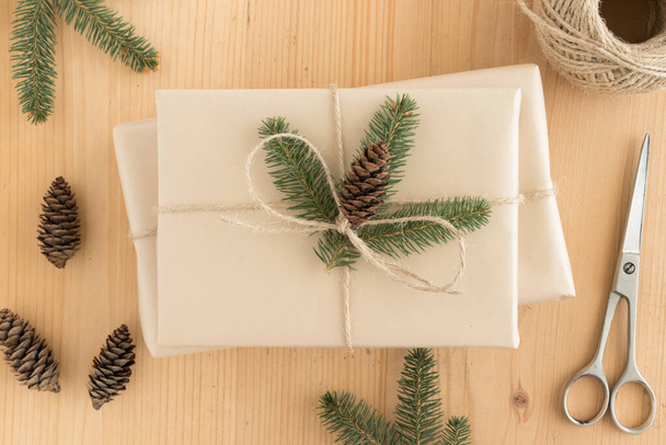 Draufsicht auf ein kraftvolles Weihnachtsgeschenk umgeben von Tannenzapfen, Blättern und Bindfäden auf einem Holztisch. - Foto, Bild