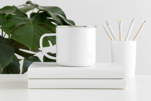Enamel mug mockup with workspace accessories and a monstera plant. - Photo, Image