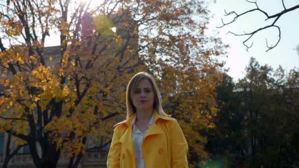 Nő köpenyben, blúz egyenesíti a haj háttér fa sárga levelek - Felvétel, videó