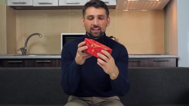 Glücklicher gutaussehender Mann begutachtet rote Schachtel, küsst, umarmt, freut sich Geschenk und lächelt - Filmmaterial, Video