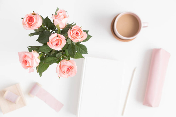 Bouquet de roses roses, livre, café et accessoires d'espace de travail sur une table blanche. Pose plate avec espace de copie vierge. - Photo, image
