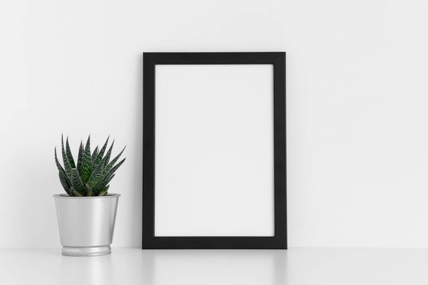 Simulacro de marco negro con un cactus en una olla sobre una mesa blanca. Orientación vertical
. - Foto, imagen