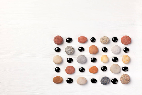 pattern of colored pebbles and black glass beads on white wooden background. Meditation and calmness concept. Flat lay, top view. copy space - Foto, afbeelding