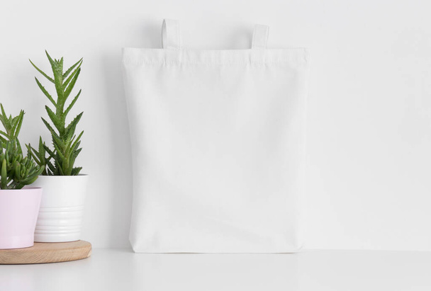 White tote bag mockup with succulents on a white table. - Фото, изображение
