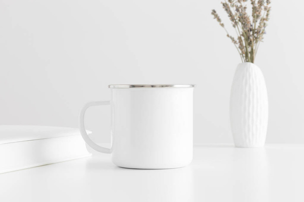 Enamel mug mockup with a lavender in a vase and a book on a white table. - Foto, afbeelding
