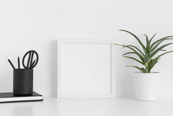 Λευκό τετράγωνο πλαίσιο mockup με μια αλόη βέρα σε μια κατσαρόλα και αξεσουάρ χώρου εργασίας σε ένα λευκό τραπέζι. - Φωτογραφία, εικόνα