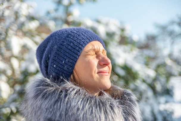 Ένα κορίτσι με μπλε ρούχα το χειμώνα σε ένα χιονισμένο πευκοδάσος απολαμβάνει την παγωμένη φύση. Χειμώνας Χριστούγεννα διάθεση. - Φωτογραφία, εικόνα